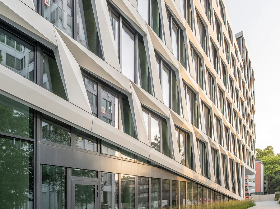 Vue latérale du bâtiment ONE PLAZA avec une façade structurée, de grandes fenêtres et un espace paysagé à l’avant.